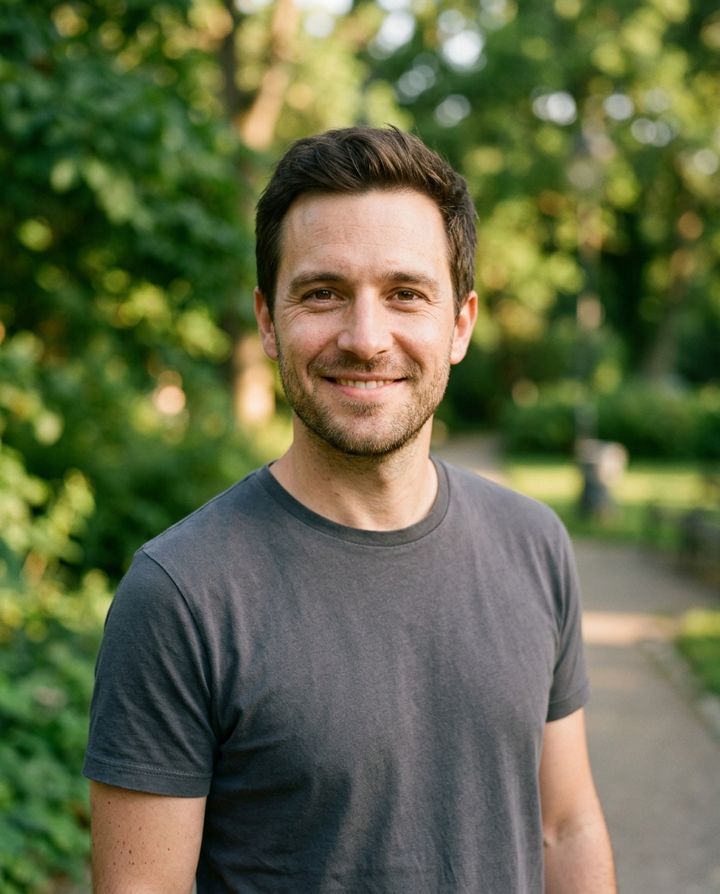 The same man smiling without sunglasses in a sunny park