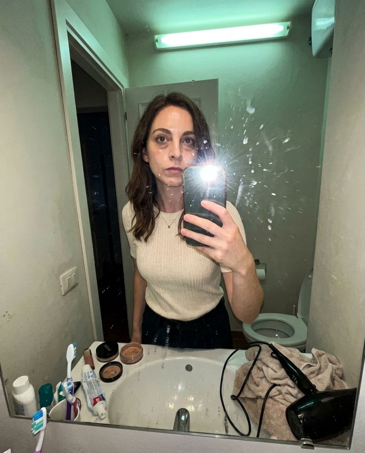 Woman taking a bathroom mirror selfie with flash glare and a cluttered sink