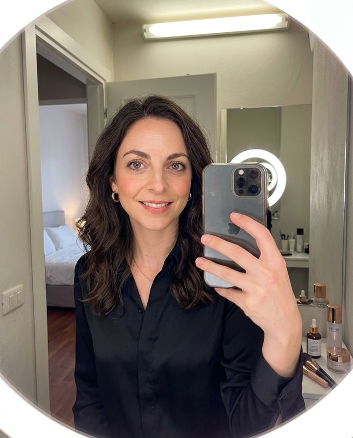 The same woman taking a mirror selfie in a tidy bathroom with soft light